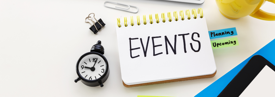 Computer keyboard, clock, and folders on a desk with a sign reading EVENTS