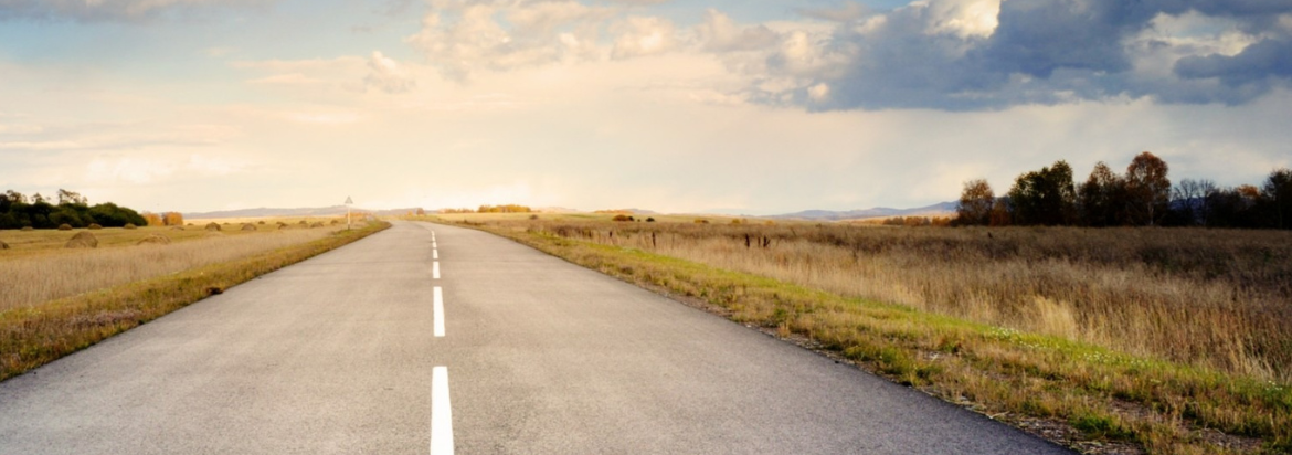 Straight road disappearing into the horizon with a wide open sky of sun and clouds