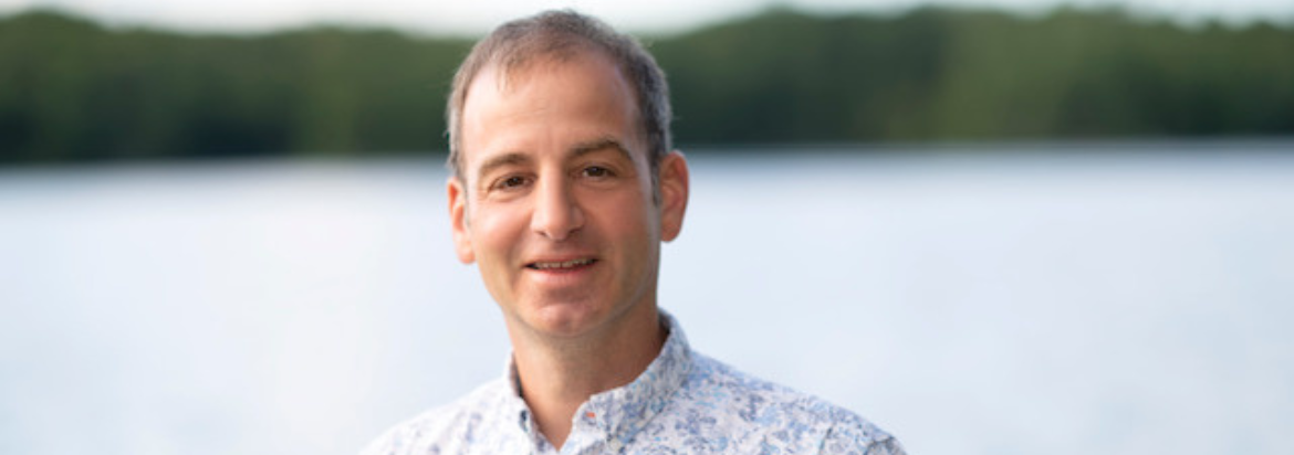 Dr. Paul Winston standing in front of a lake with trees in the background