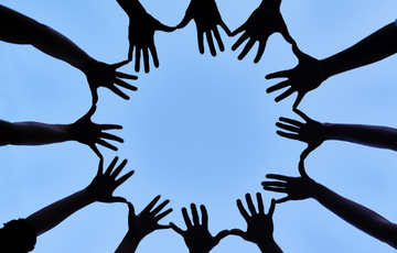 a circle of hands touching in front of a blue sky